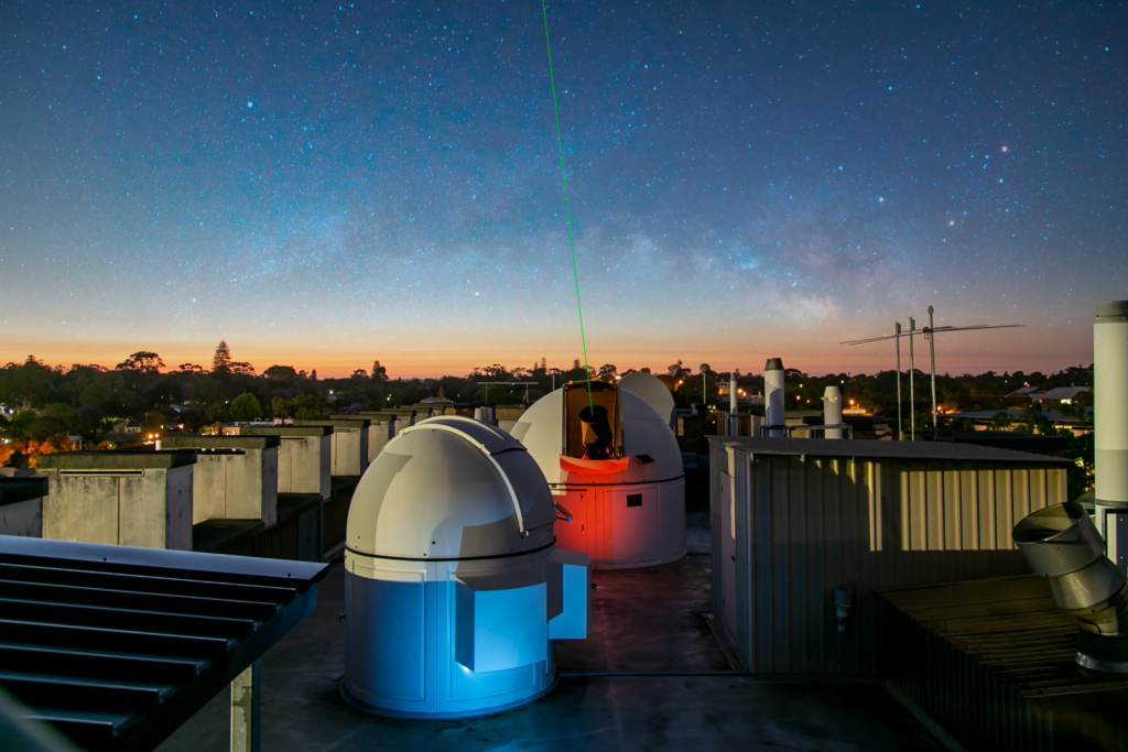 Rooftop observatories at dusk with a laser pointing to the sky.