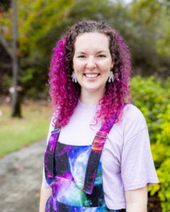 Dr Kat Ross, with pink hair and a space-themed overalls, stands outside Curtin university.