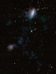 A large bright galaxy, top, and a small faint galaxy, bottom, with a faint cloudy stream of gas connecting them.